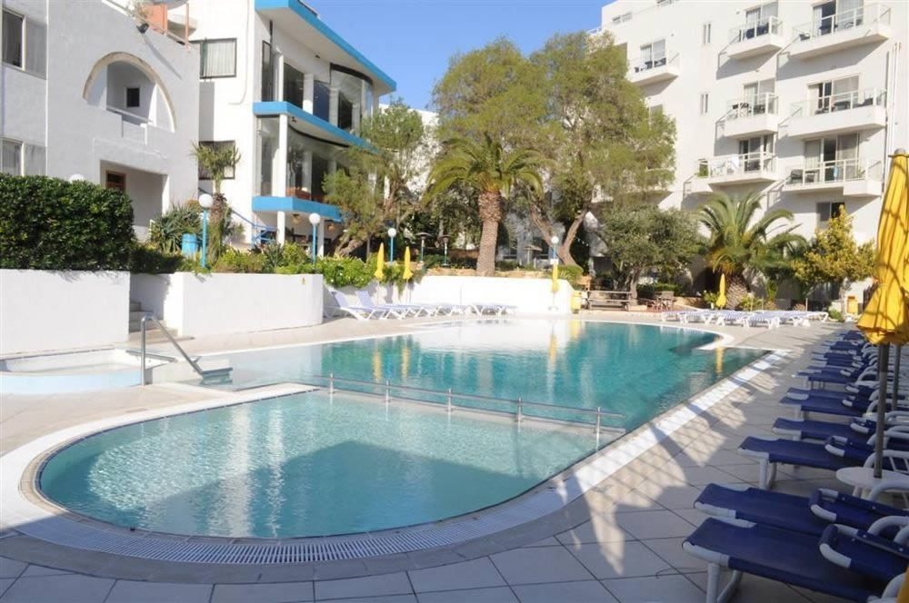 Outdoor swimming pool with sun loungers and parasols in a white apartment complex courtyard at Salina Wharf, Malta