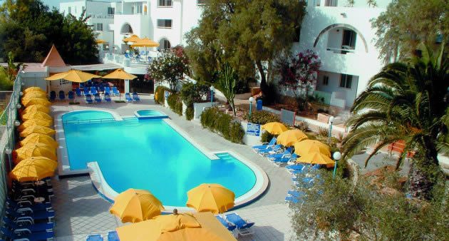 Outdoor resort swimming pool surrounded by yellow parasols and blue sun loungers beside white apartment buildings