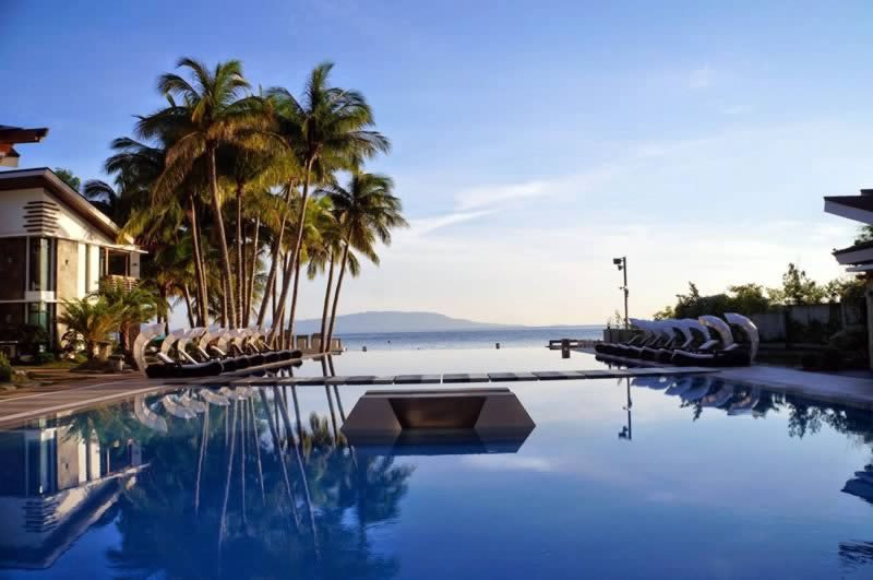 Infinity pool at a seaside resort with palm trees and rows of sun loungers overlooking the ocean at sunset