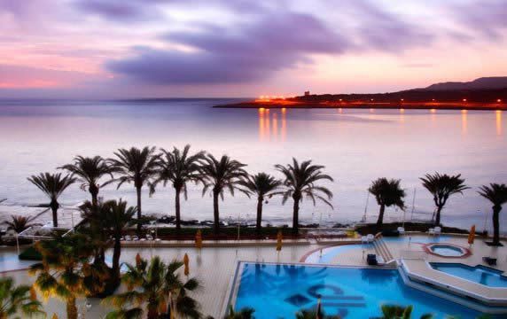 Sunset view over a calm sea with palm trees and a resort swimming pool in the foreground