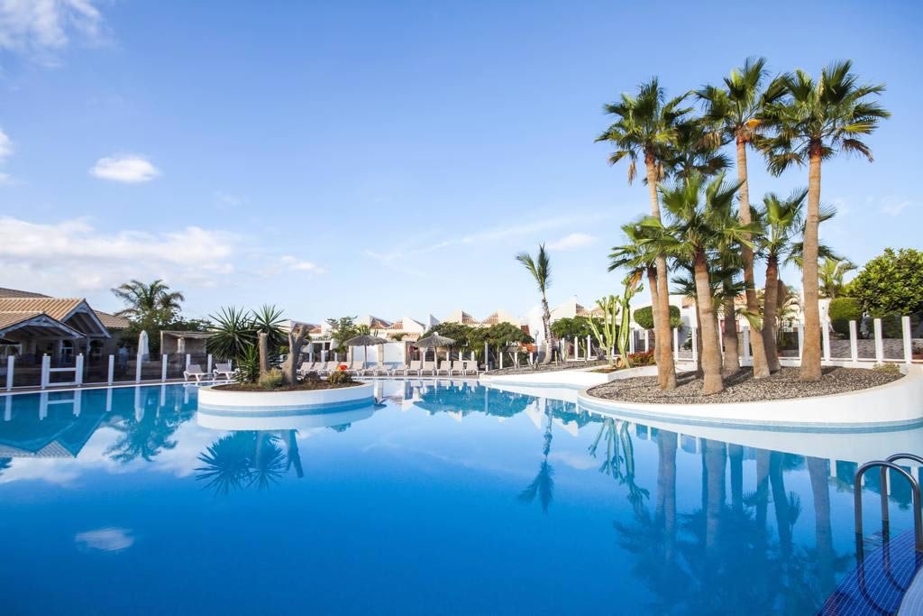 Outdoor resort swimming pool with palm trees, sun loungers and clear blue sky in Tenerife