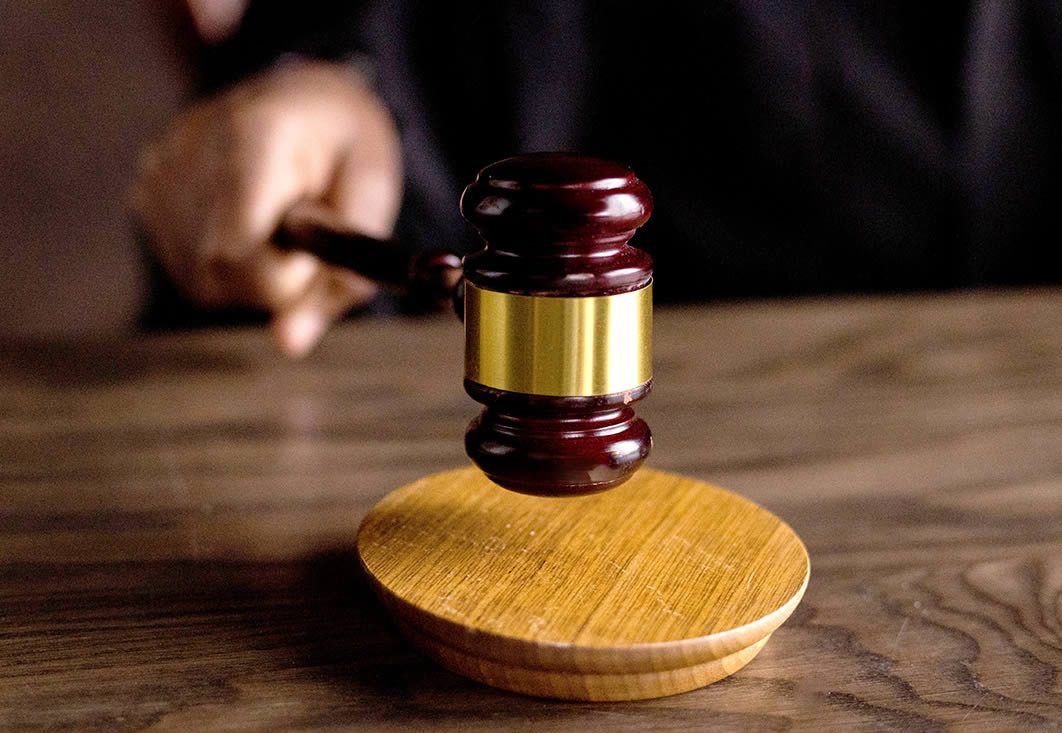 Close-up of a judge’s gavel above a wooden sound block on a desk, with a blurred hand in the background