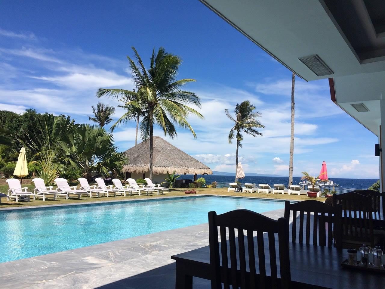 Outdoor swimming pool with sun loungers, parasols and palm trees overlooking the sea at a holiday resort