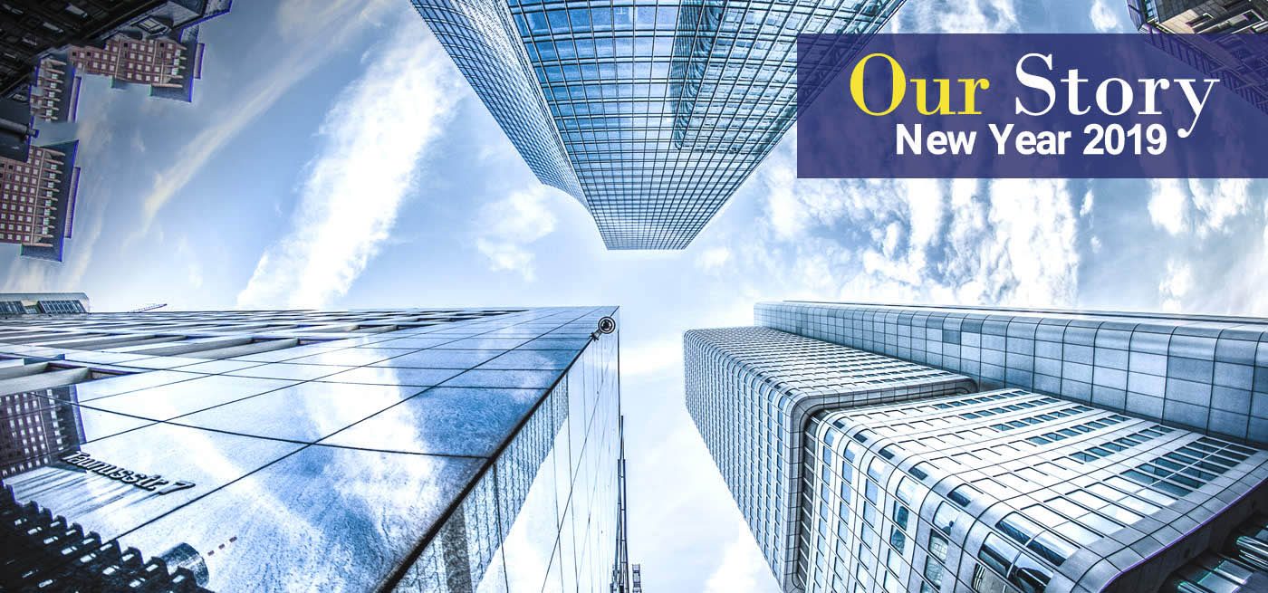 Upward view between modern glass skyscrapers against a blue sky, with the text “Our Story New Year 2019”