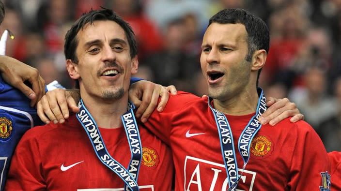 Two Manchester United footballers in red shirts wearing Barclays medals, celebrating with arms around each other on the pitch