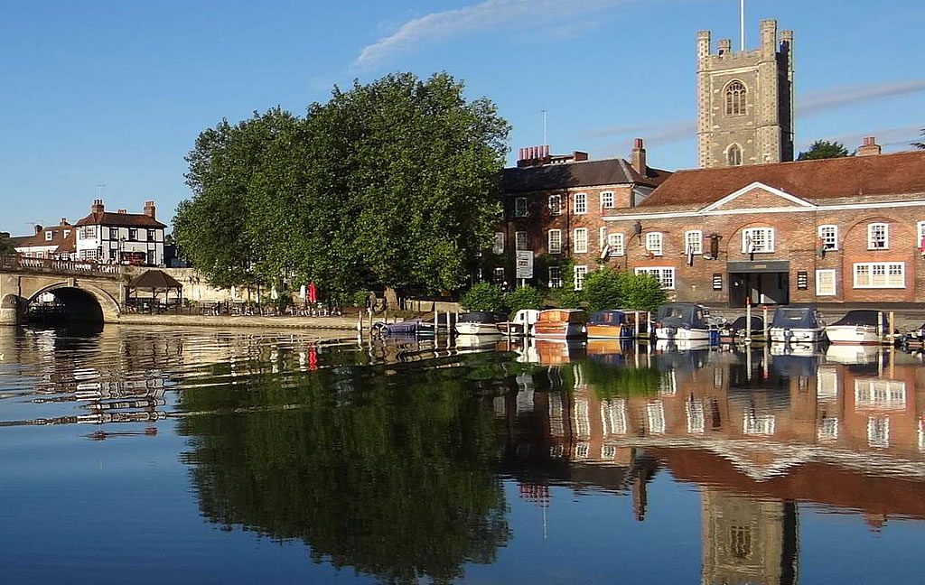 Riverside view in Henley-on-Thames with moored boats, historic buildings and church tower reflected in the River Thames on a clear day