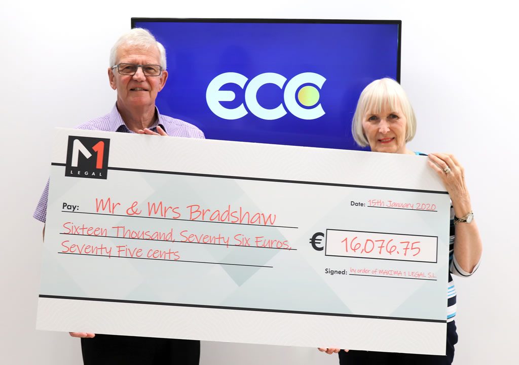 Older couple holding a large presentation cheque for €16,076.75, with ECC and M1 Legal logos in the background
