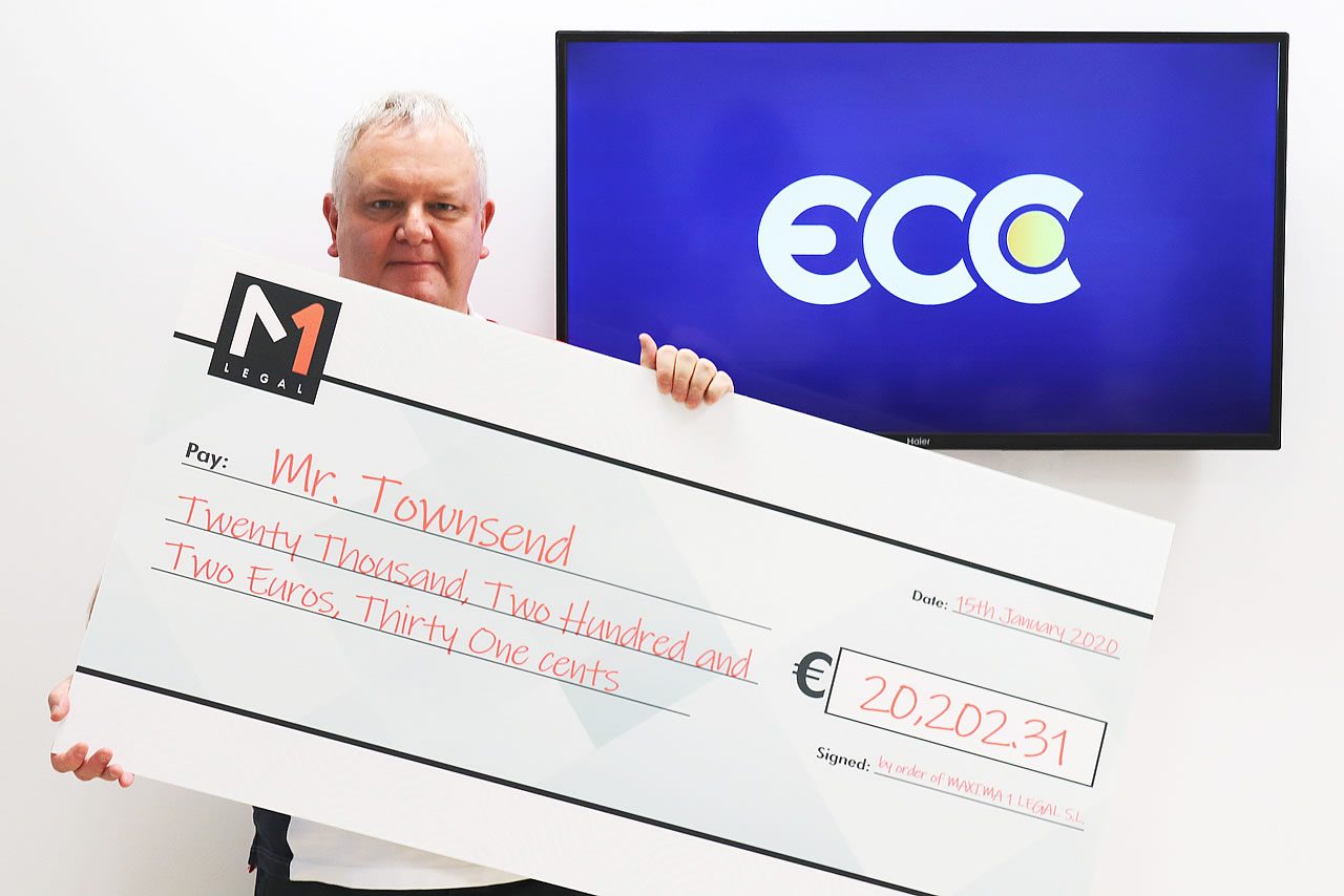 Man holding an oversized cheque for €20,202.31 made out to Mr Townsend, with M1 Legal branding and a screen behind displaying the ECC logo