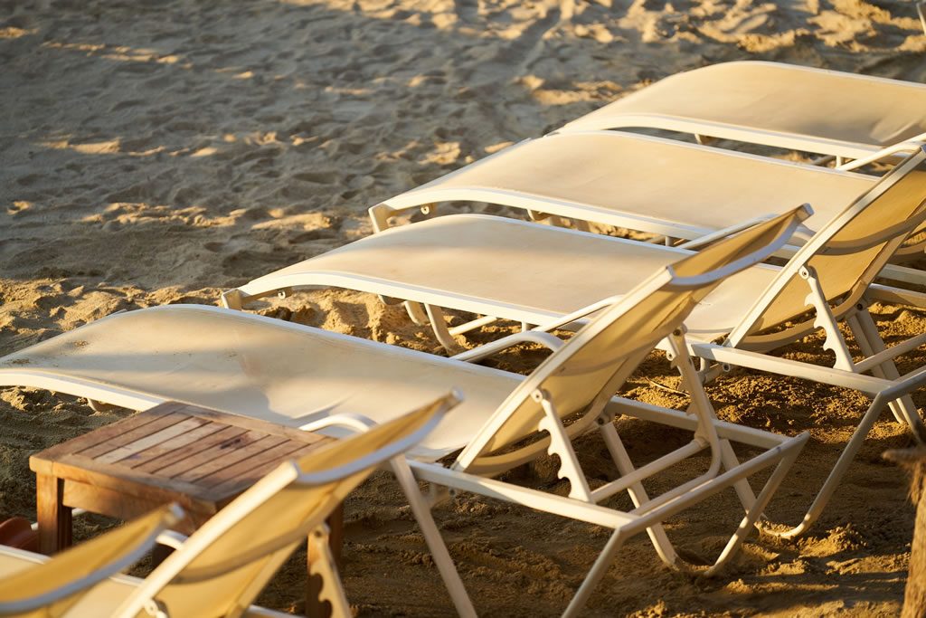 Empty sun loungers lined up on a sandy beach in warm sunlight