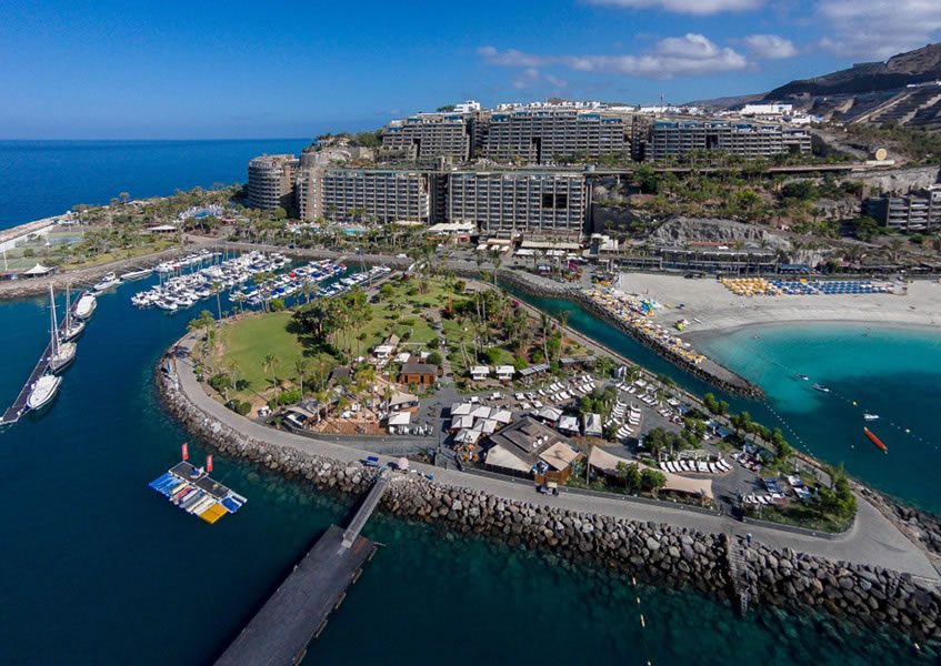 Aerial view of a coastal resort complex with marina, beach and hillside apartment blocks by the sea in Gran Canaria