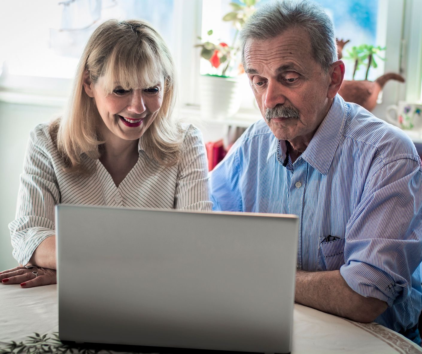 Older couple sitting at a table looking at a laptop screen, reading a timeshare relinquishment waiver online