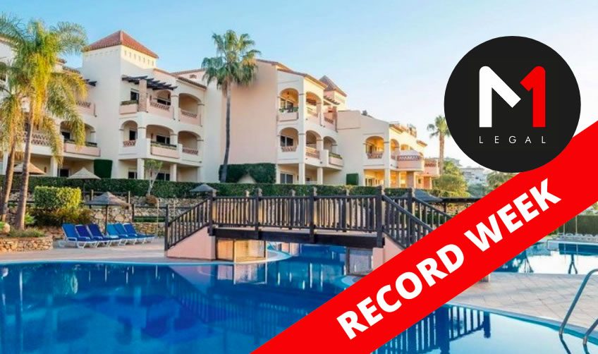 Outdoor swimming pool and bridge in front of a white holiday apartment complex with palm trees, overlaid with an M1 Legal logo and “RECORD WEEK” banner
