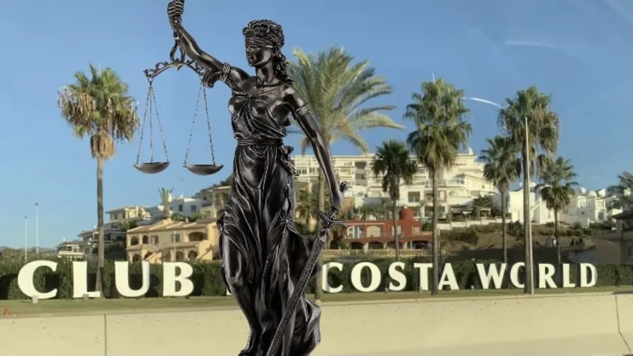 Statue of Lady Justice holding scales in front of a Club La Costa World sign with palm trees and resort buildings in the background