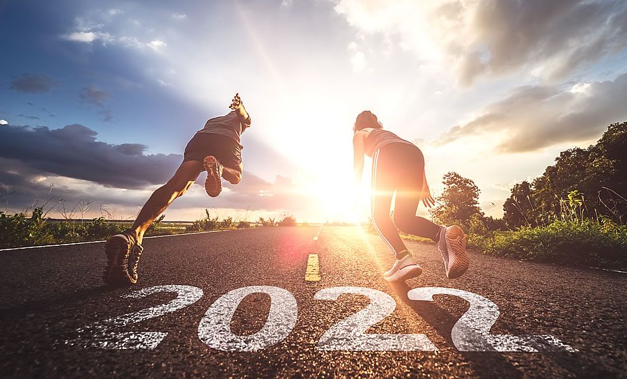 Two runners sprinting down a road marked “2022” towards the sunrise under a cloudy sky