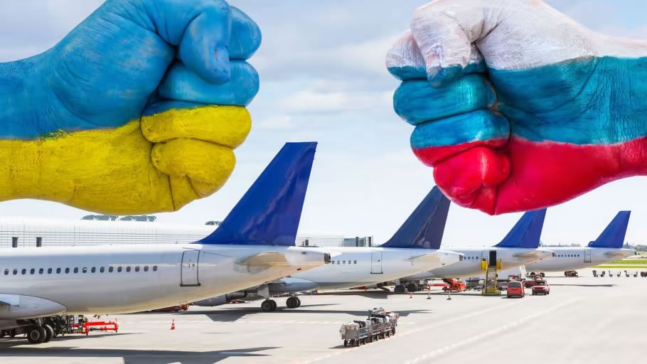 Painted fists in Ukraine and Russia flag colours facing each other above parked passenger aeroplanes on an airport tarmac