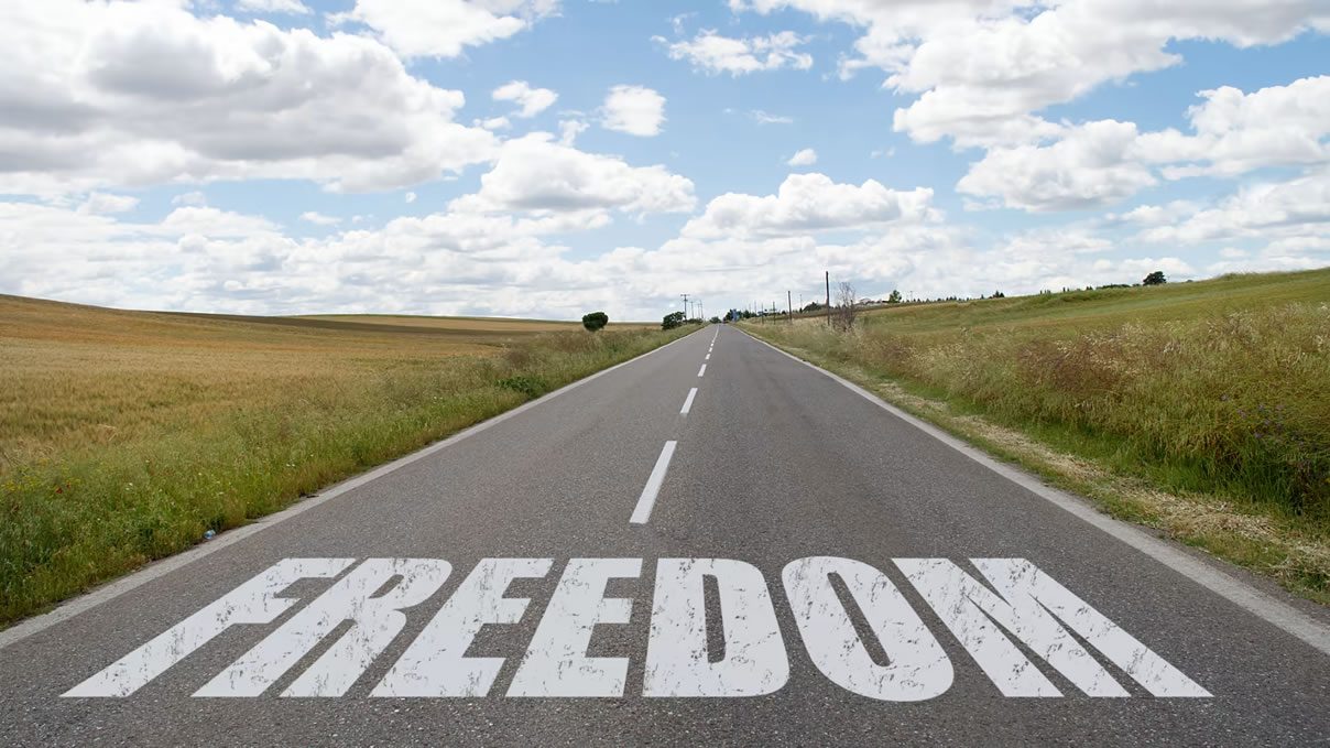 Long straight country road under a cloudy blue sky with the word “FREEDOM” painted across the tarmac in large white letters