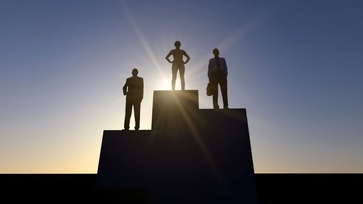 Silhouettes of three businesspeople standing on winners podium steps against a sunburst sky at sunset