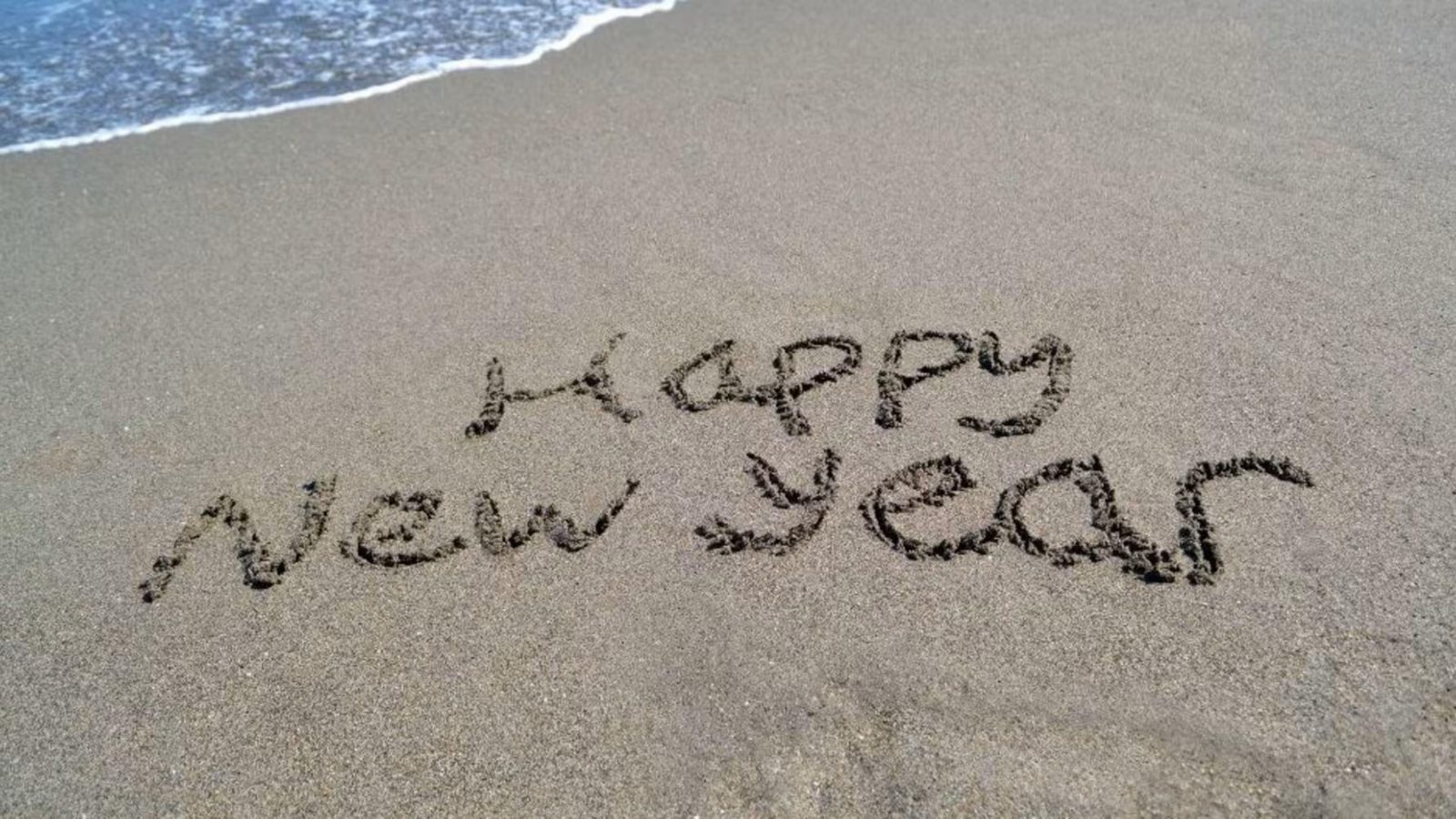 Happy New Year written in the sand on a beach beside the shoreline