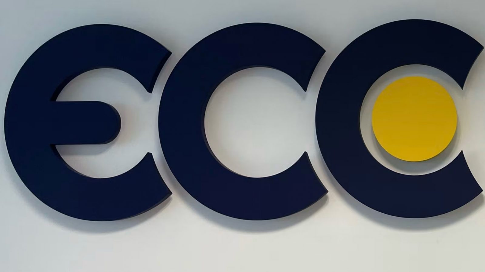 Close-up of the ECC logo in dark blue lettering with a yellow circle on a white wall