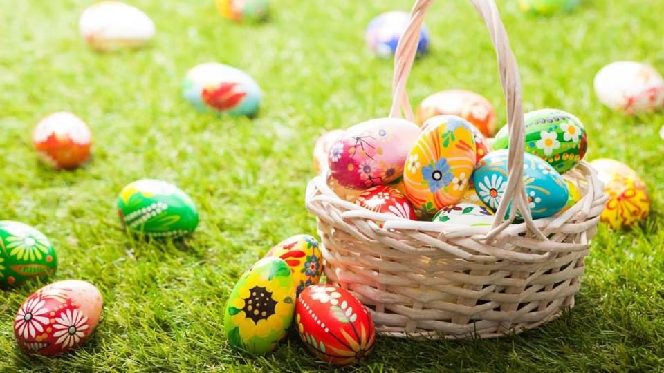 Basket of colourful painted Easter eggs on green grass with more eggs scattered around outdoors