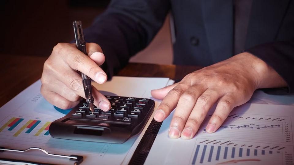 Close-up of a person using a calculator and pen over financial charts and paperwork, illustrating timeshare economics cost comparison calculations