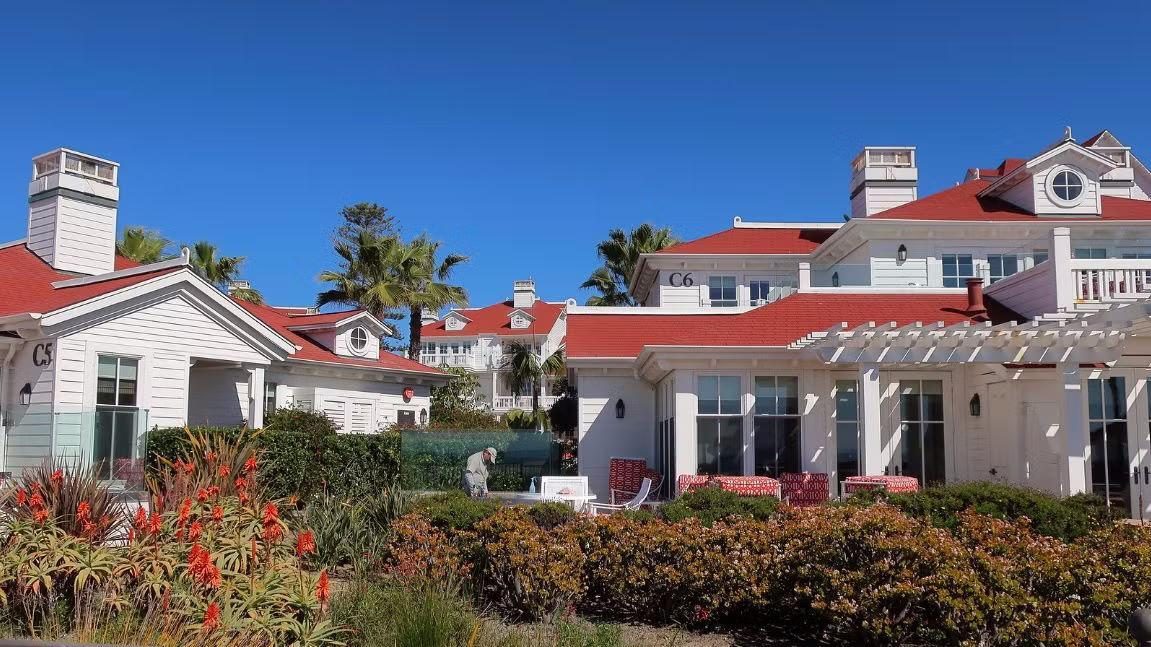 Holiday resort buildings with red roofs and white cladding, palm trees and landscaped gardens under a clear blue sky