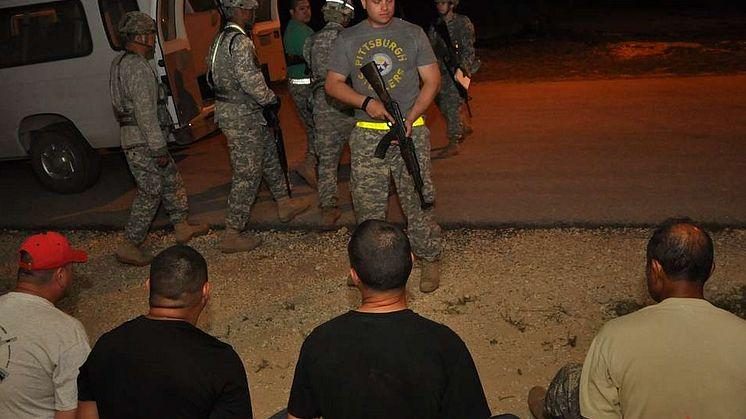 Soldiers with rifles stand guard beside detained men sitting on the ground at night near a vehicle in Mexico