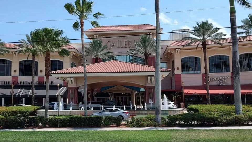 Exterior of The Galleria mall in Fort Lauderdale, with palm trees, fountains and the “GALLERIA” sign above the entrance
