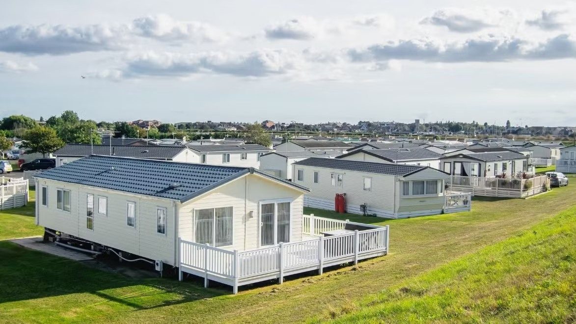 Row of static caravans on a UK holiday park, with white decking on a grassy slope under a cloudy sky