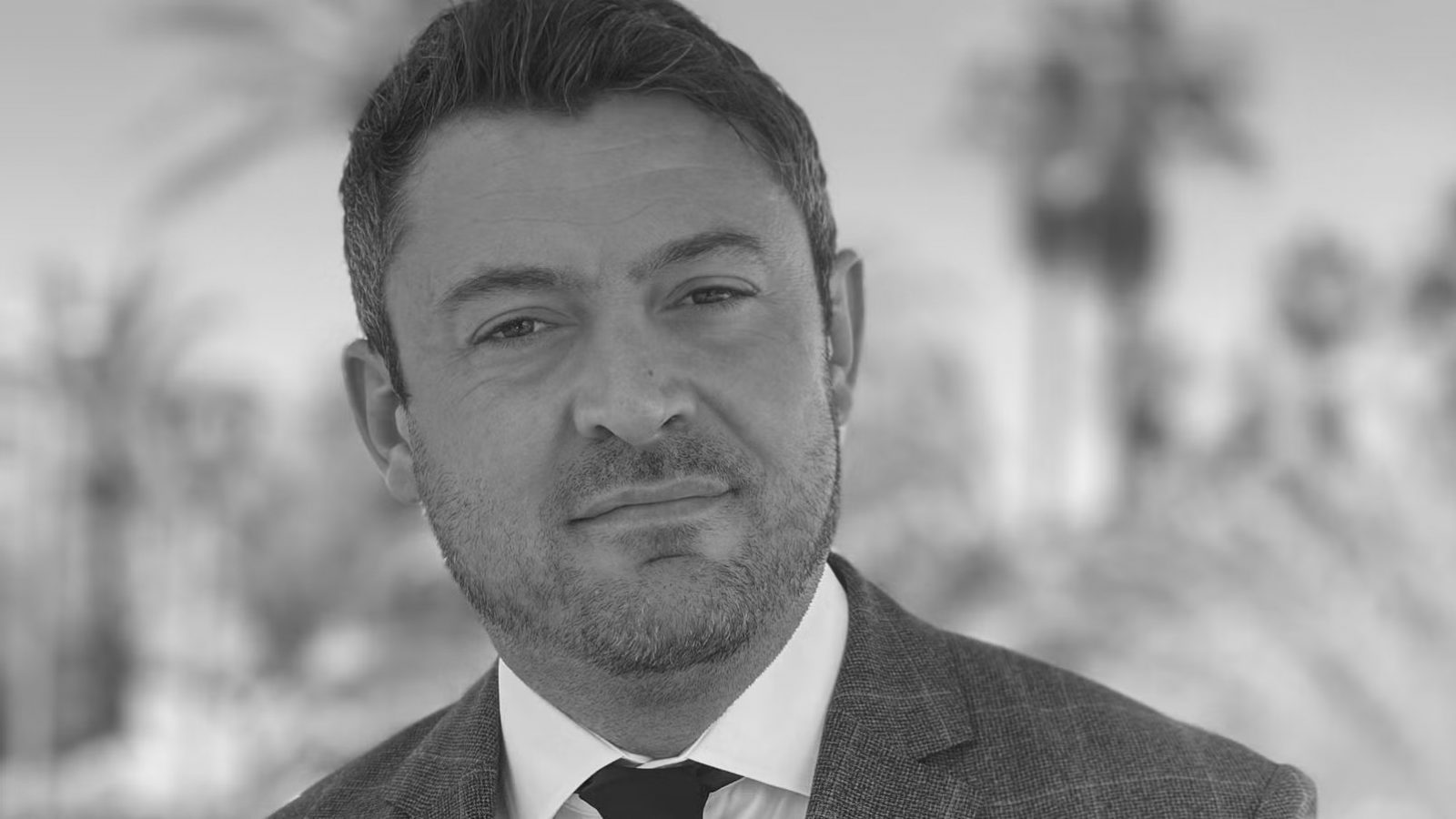 Black-and-white head-and-shoulders portrait of European Consumer Claims CEO Greg Wilson in a suit and tie with a blurred office background