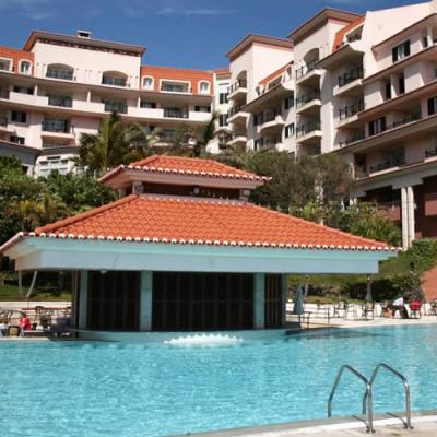 Outdoor swimming pool with a tiled roof pavilion and the Madeira Regency Palace hotel building in the background, Portugal