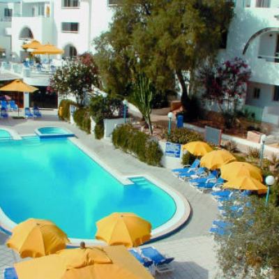 Outdoor resort swimming pool surrounded by yellow parasols and blue sun loungers beside white apartment buildings