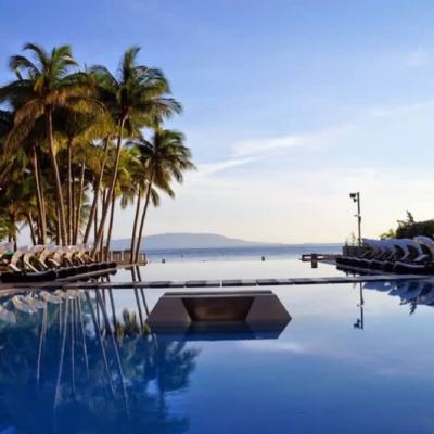 Infinity pool at a seaside resort with palm trees and rows of sun loungers overlooking the ocean at sunset