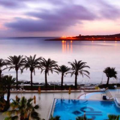 Sunset view over a calm sea with palm trees and a resort swimming pool in the foreground