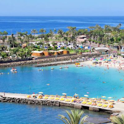 Aerial view of a seaside resort with a sandy beach, palm trees, sun loungers, a sheltered lagoon and hotels by the ocean