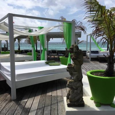 Beachfront resort deck with white cabanas, green curtains and potted palms overlooking the sea