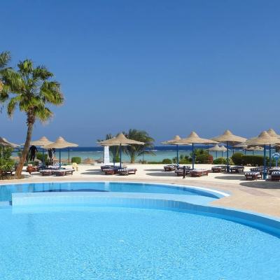 Outdoor resort swimming pool with sun loungers and straw parasols beside the sea under a clear blue sky