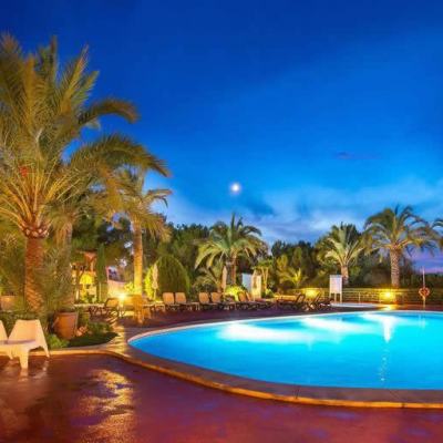 Illuminated resort swimming pool at dusk with palm trees, sun loungers and a deep blue sky in Cala Pi, Majorca