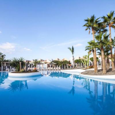 Outdoor resort swimming pool with palm trees, sun loungers and clear blue sky in Tenerife