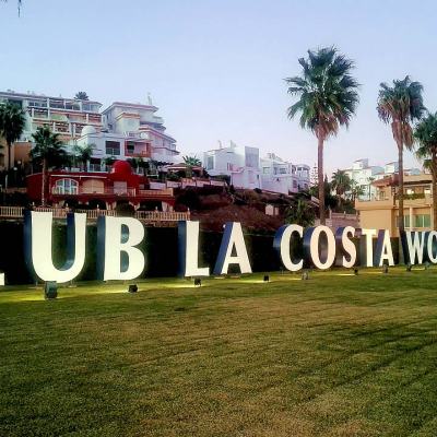 Large “CLUB LA COSTA WORLD” sign on a grass lawn with palm trees and resort buildings in the background