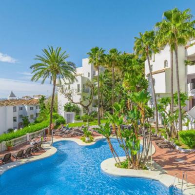 Outdoor resort swimming pool with sun loungers, palm trees and white apartment buildings under a clear blue sky in Spain