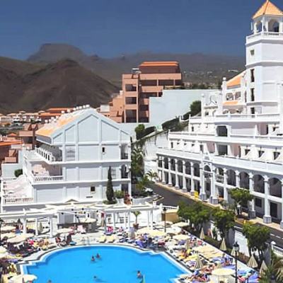 Large hotel complex with balconies beside an outdoor swimming pool and sun loungers, with mountains in the background in Spain