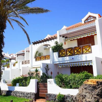 White Mediterranean resort apartments with balconies and striped awnings, palm tree and garden under a clear blue sky in Spain