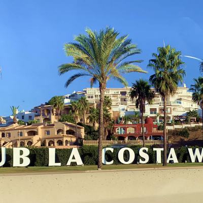 Large “CLUB LA COSTA WORLD” sign in front of palm trees and resort buildings under a clear blue sky in Spain