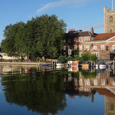 Riverside view in Henley-on-Thames with moored boats, historic buildings and church tower reflected in the River Thames on a clear day