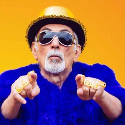 Older man wearing sunglasses and a yellow hat, pointing at the camera against a bright yellow background