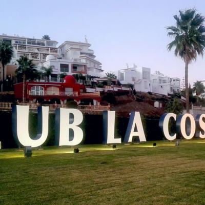 Large “CLUB LA COSTA WORLD” sign on a lawn with palm trees and resort apartment buildings in the background
