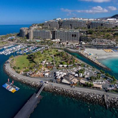 Aerial view of a coastal resort complex with marina, beach and hillside apartment blocks by the sea in Gran Canaria