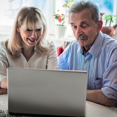 Older couple sitting at a table looking at a laptop screen, reading a timeshare relinquishment waiver online
