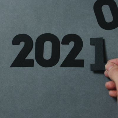 Hand placing a black number 1 next to “2020” to form “2021” on a grey background